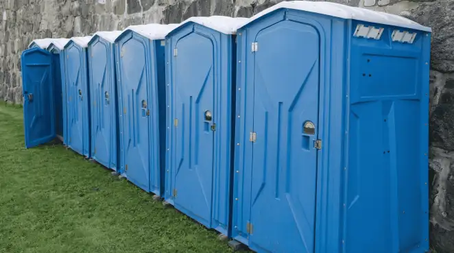 Row of blue portable toilets lined up on grass against a stone wall for event sanitation in Colorado Springs, CO