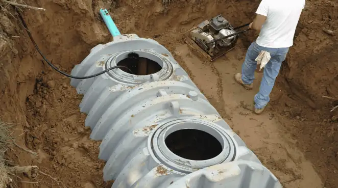 Septic tank installation showing a technician compacting soil around a new poly septic tank in an excavation pit in Colorado Springs, CO